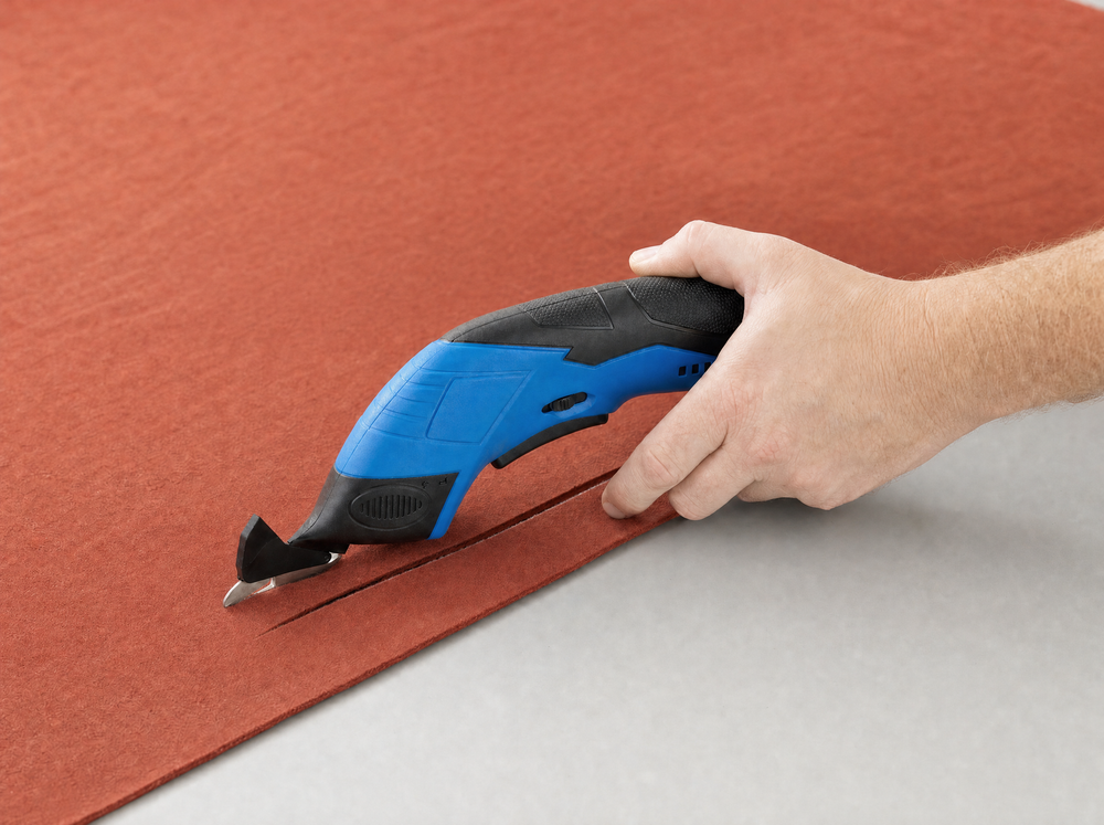 Distinct top-right close photograph of right hand guiding exact blue shears into cream cotton at a long straight chalk line